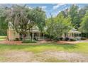 Charming home featuring a light yellow exterior, green metal roof, spacious porch, and lush landscaping with mature trees at 6200 Us-401 S, Bunnlevel, NC 28323