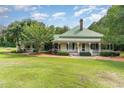 Charming home featuring a light yellow exterior, green metal roof, spacious porch, and lush green lawn at 6200 Us-401 S, Bunnlevel, NC 28323