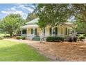 Charming home showcasing a light yellow exterior, green metal roof, spacious porch with chairs and lush landscaping at 6200 Us-401 S, Bunnlevel, NC 28323