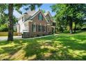 A side view of the brick home featuring a sprawling green lawn with mature tree shade and a garage at 3811 Cottonwood Dr, Durham, NC 27705