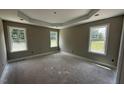 Spacious main bedroom with tray ceiling, neutral paint, and three windows overlooking the front yard with unfinished floors at 2776 Rains Mill Rd, Princeton, NC 27569