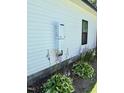 Modern tankless water heater on exterior of home with flowering hostas at 451 N Lincoln St, Benson, NC 27504