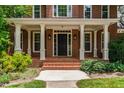 Inviting front porch with white columns, brick steps, and a black front door surrounded by sidelights and transom window at 5123 Richland Dr, Raleigh, NC 27612