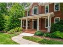 Charming brick home featuring a welcoming front porch with white columns, brick steps and walkway, and lush landscaping at 5123 Richland Dr, Raleigh, NC 27612