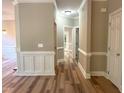 Hallway with white wainscoting, neutral walls, wood-look flooring, and doors leading to various rooms of the home at 8100 Laurel Mountain Rd, Raleigh, NC 27613