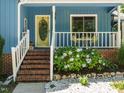 Inviting porch featuring a yellow front door, white railings, and colorful flower landscaping around the brick base at 1487 Kentucky Ave, Sanford, NC 27332
