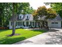 Beautiful home featuring a manicured lawn, mature tree, black shutters, white siding, and a driveway leading to an attached garage at 8604 Timberwind Dr, Raleigh, NC 27615