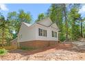 Rear exterior view of a home featuring white siding, a brick foundation, and lush, mature trees at 1952 Lewis Dr, Burlington, NC 27215