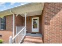 Traditional brick home's front porch features a white railing and trim, and a glass paneled front door at 1822 Atterbury Ln, Durham, NC 27712
