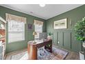 This home office features wainscoting, two windows, a wooden desk, and hardwood floors with a patterned rug at 158 Arlie Ln, Lillington, NC 27546