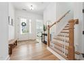 Bright foyer featuring hardwood floors, a staircase with white railings, and a glimpse into other rooms at 237 Emory Bluffs Dr, Holly Springs, NC 27540
