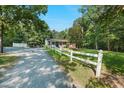 View of the home and white fence, nestled between trees, with a gravel driveway and carport at 904 Lanier Farm Rd, Sanford, NC 27330