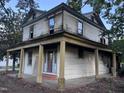 Two-story home featuring peeling paint, mature trees, and a covered front porch with columns at 12670 School House Rd, Middlesex, NC 27557