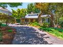 Home featuring stone accents, a metal roof, covered porch, and mature trees lining the driveway at 2707 Anderson Drive Dr, Raleigh, NC 27608