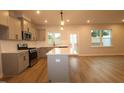 A well-lit kitchen featuring gray cabinets, stainless steel appliances, an island and wood flooring extends to dining area at 920 Montague Ave, Durham, NC 27703