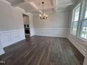 Elegant dining room featuring wainscoting, coffered ceiling, dark wood floors, and modern chandelier at 3509 Bailey Lake Dr, Fuquay Varina, NC 27526