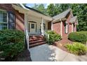 Inviting front porch with brick steps, white railings, and a decorative front door, surrounded by lush greenery at 745 Oaks Lane Rd, Timberlake, NC 27583