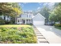 Inviting two-story home featuring a classic front porch, attached garage, and a sloped driveway amidst lush greenery at 302 Caraway Ln, Cary, NC 27519
