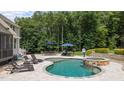 A luxury pool with a lounge area, outdoor dining, and stone-clad hot tub are surrounded by lush landscaping at 7410 Chouder Ln, Wake Forest, NC 27587