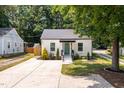 A quaint white home with green door, complemented by a concrete driveway and landscaped front yard at 3649 Guess Rd, Durham, NC 27705