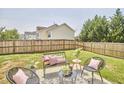 Cozy backyard patio seating area with chairs, pillows, and a modern-style coffee table on lush grass with privacy fence at 418 Magna Dr, Durham, NC 27703