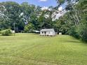 White home with metal carport on large grassy lot, surrounded by lush, mature trees and blue skies at 229 Maple Dr, Oxford, NC 27565