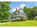 White two-story home featuring a welcoming front porch, black shutters, and green lawn with mature shade trees at 401 N Main St, Louisburg, NC 27549