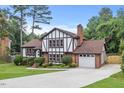 Charming Tudor-style home with brick and white facade, lush lawn, and a paved driveway leading to a garage at 2020 Port Royal Rd, Raleigh, NC 27609