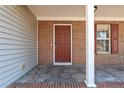 Close-up of a home's entrance with brick accents, a dark red front door, and a patterned concrete porch at 140 Cobblestone Dr, Spring Lake, NC 28390