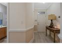 Inviting hallway with light wood flooring, leading to a white front door and featuring a console table with a decorative lamp at 159 Gallery Dr # 103, Spring Lake, NC 28390