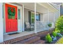 Close-up of front porch with a bright red door, rocking chair, and landscaped flower bed at 191 Trenton Pl, Cameron, NC 28326