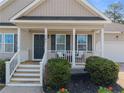 Close-up of a covered front porch with white railing, black door, and manicured greenery at 187 Gunner Ct, Broadway, NC 27505