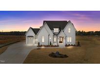 Beautifully landscaped modern farmhouse with a three-car garage, set against a picturesque sunset backdrop at 4909 Hidden Pasture Way, Zebulon, NC 27597