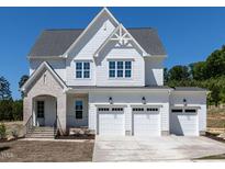 Two-story white home boasts a three-car garage, manicured lawn, and elegant architectural details at 6048 Scalybark Rd, Durham, NC 27712