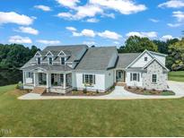 Beautiful white home with stone accents, a welcoming porch, and lush green lawn and a scenic lake view at 1618 Ben Wilson Rd, Mebane, NC 27302