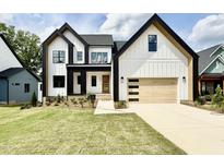 Modern farmhouse with black trim, white siding, wood garage door, and green lawn at 205 Red Cardinal Ct, Youngsville, NC 27596