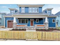 Charming blue two-story home boasts stone accents, a welcoming front porch, and a quaint yellow picket fence at 417 E Moore St, Apex, NC 27502