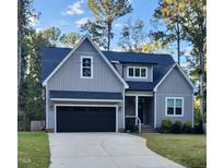 Charming two-story home with a black garage door, gray siding and a well-manicured front yard and concrete driveway at 209 Choctaw Dr, Louisburg, NC 27549