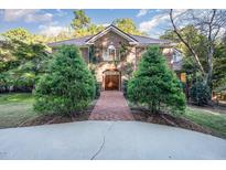 Elegant brick home with mature evergreens and a brick walkway leading to a grand arched wooden doorway at 107 Silo Dr, Chapel Hill, NC 27514