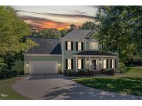 Two-story light green house with a gray roof, white garage door, and manicured lawn at sunset at 11308 Timbergrove Ln, Raleigh, NC 27614