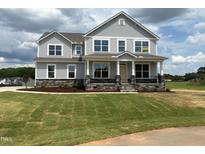 Beautiful two-story home featuring stone accents, a welcoming front porch, and lush green lawn at 111 Demascus Way # 021, Four Oaks, NC 27524