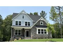 Charming two-story home with stone accents, covered porch, and a well-manicured lawn surrounded by lush trees at 684 Magnolia Acres Ln, Fuquay Varina, NC 27526