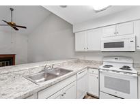 Bright kitchen featuring white appliances, cabinets, and countertops overlooking a living area with vaulted ceiling and fireplace at 14 Stone Village Ct, Durham, NC 27704