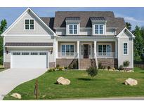 Inviting home featuring a manicured lawn, covered porch, brick accents and a white garage door at 1233 Azalea Garden Cir, Raleigh, NC 27603