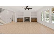 Bright living room featuring a fireplace, built-in shelving, ceiling fan and large windows at 617 Darian Woods Dr, Holly Springs, NC 27540