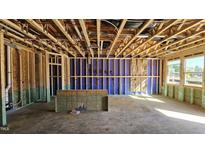 Unfinished living room featuring exposed framing, utilities, and a sunlit view through the windows at 3858 Well Fleet Drive, Willow Springs, NC 27592