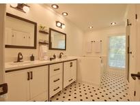 Well-lit bathroom featuring double vanity, white cabinets, and contrasting black and white hexagon tile flooring at 340 Andrews Store Rd, Pittsboro, NC 27312