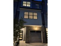 Modern townhome with a gray garage door and brick accents, illuminated by an outdoor light fixture at 702 Portia Way, Homesite 16, Morrisville, NC 27560