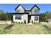 New two-story home featuring stone accents, gray siding, a manicured lawn, and a lush green wooded backdrop at 135 Cherry Bark Dr, Youngsville, NC 27596