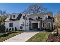 A charming two-story home with stone and white brick exterior, a three-car garage, and a manicured lawn at 1307 Mayfair Rd, Raleigh, NC 27608